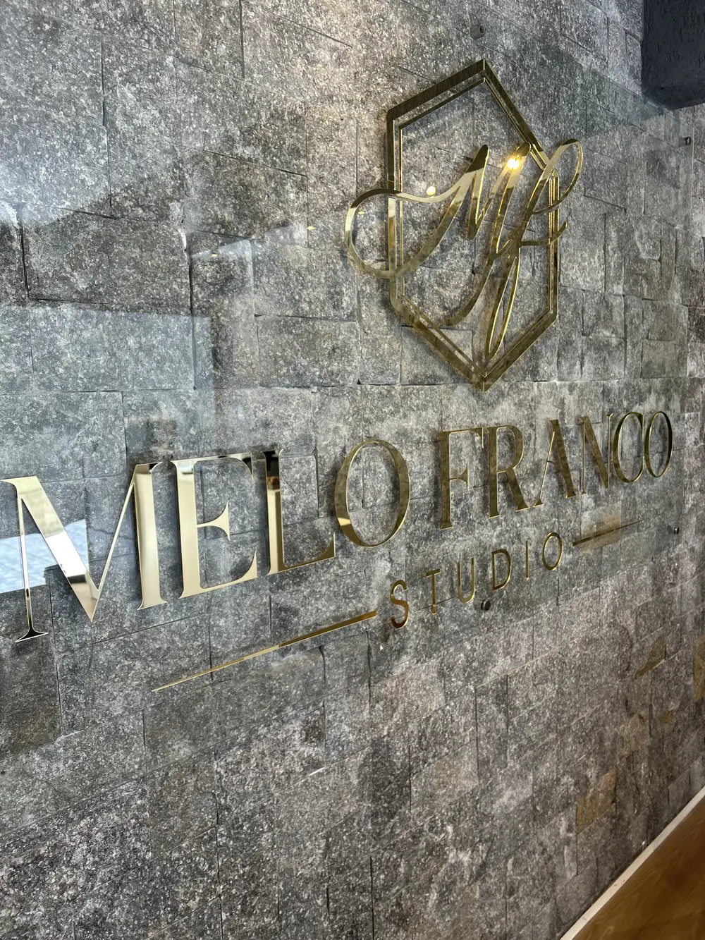 Recepção do Melo Franco Studio, com o logo dourado na parede de pedra